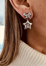 Load image into Gallery viewer, Close-up of a person wearing silver star-shaped earrings with a bow detail.